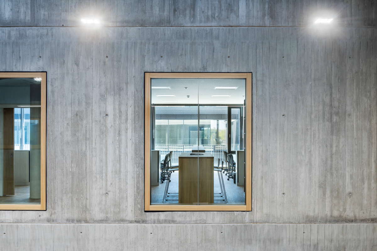 Fassadendetail im Foyer mit Fenster, eingefasst in einem starken Holzrahmen in Sichtbeton, Durchblick zum Lehrerzimmer