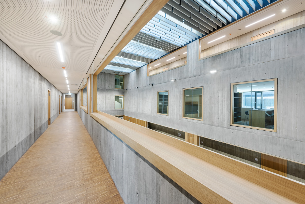 Flurgang im Obergeschoss mit Blick in den offenen Raum der Aula, Materialien Holz und Sichtbeton