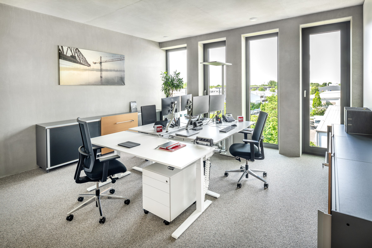 modernes Büro mit Sichtbeton für drei Personen und hohen Fenstern