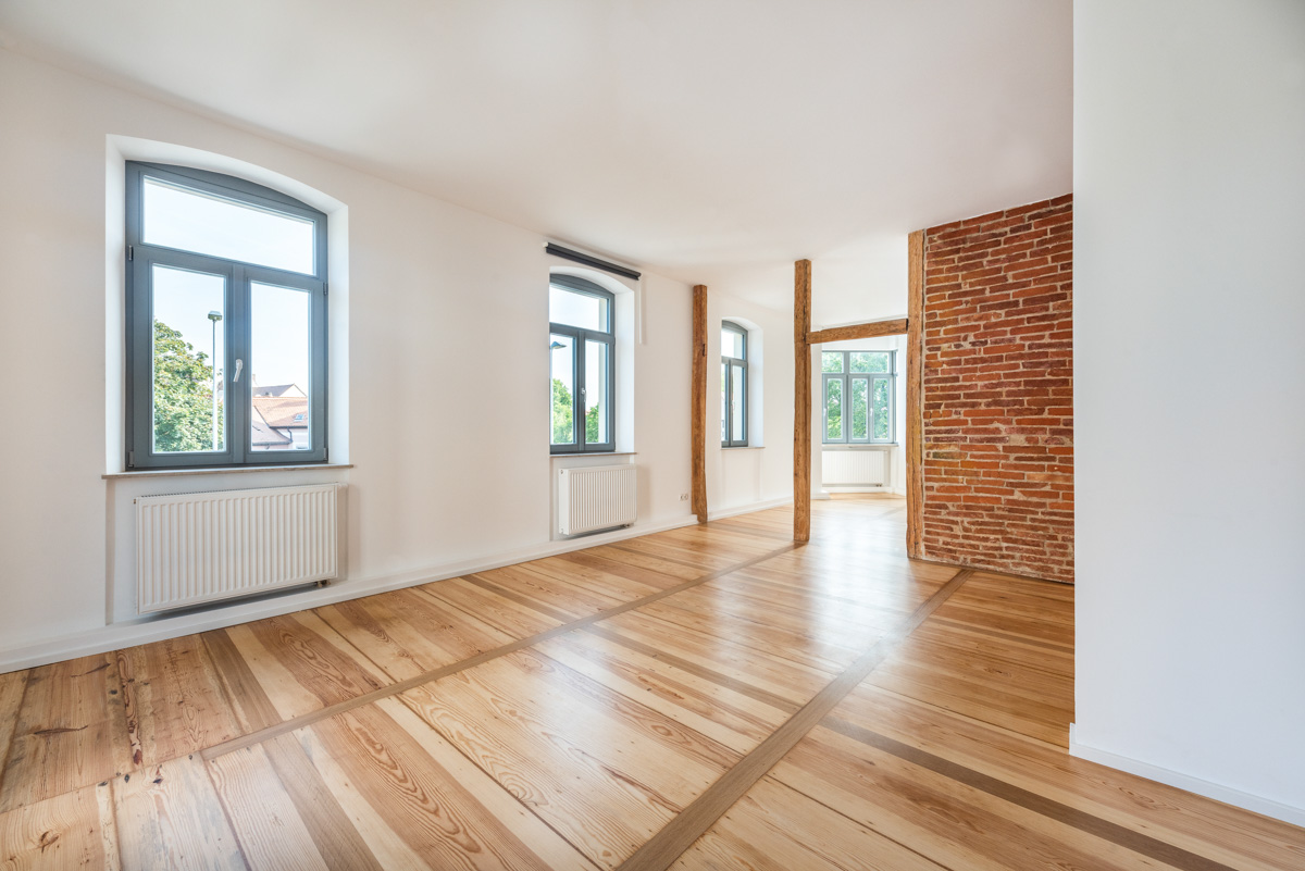 Wohnzimmer mit Dielenboden, roter Backsteinwand und Holzbalken in saniertem Altbau